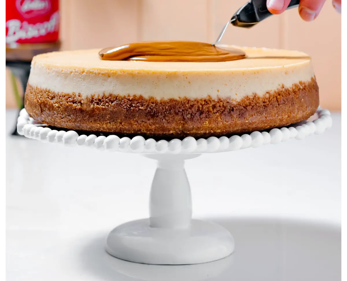 spreading cookie butter glaze on cheesecake